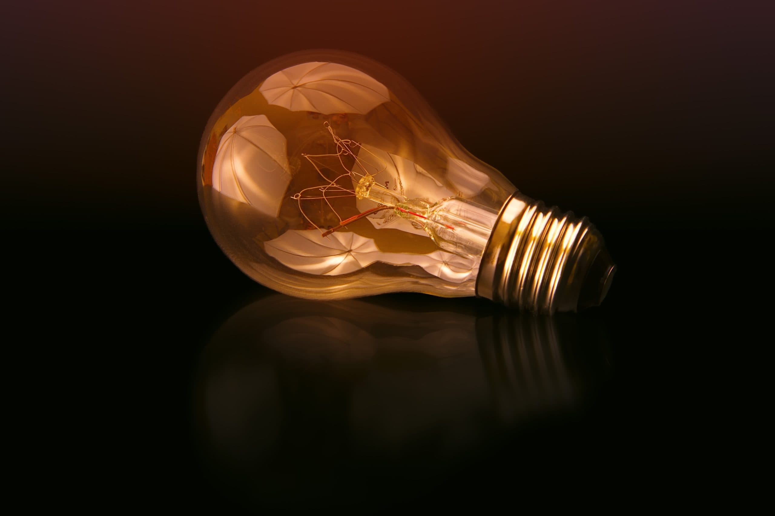 A glowing filament light bulb lying on a dark surface